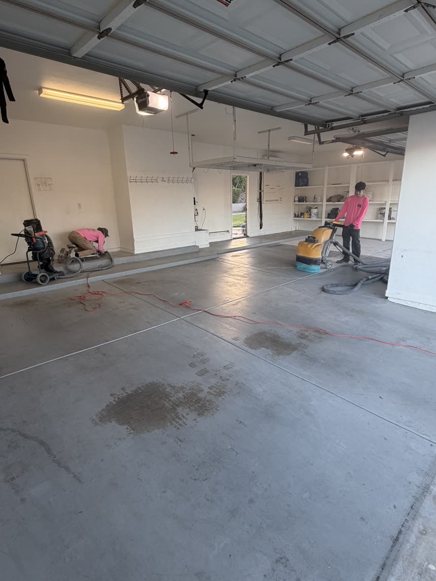 Bare concrete garage floor with an oil stain, crew grinding the slab on day one